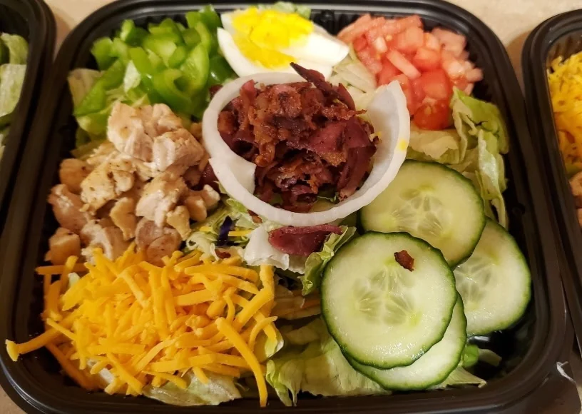 Salad topped with chicken, bacon, egg, cheese, cucumber and tomato